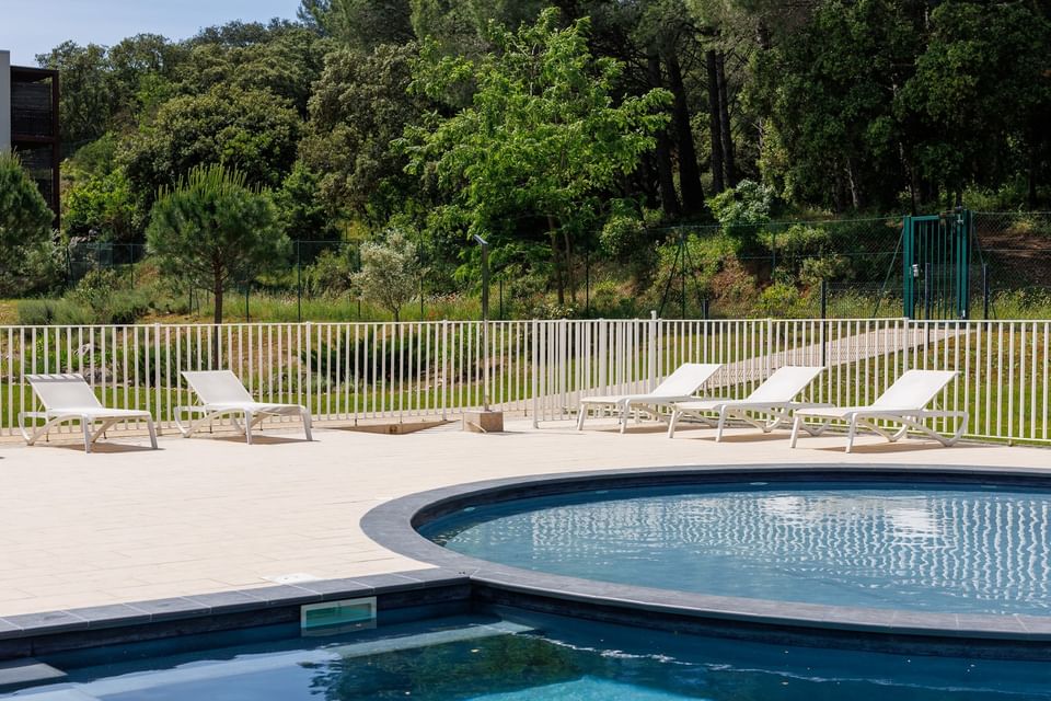 Lounge chairs on a paved deck by a semi-circular pool at ResidHotel Pont du Gard, an apartment hotel with swimming pool