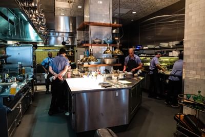 Chefs and kitchen staff preparing food inside the Ciaorigato Restaurant with stainless steel counters at Hotel Bijou