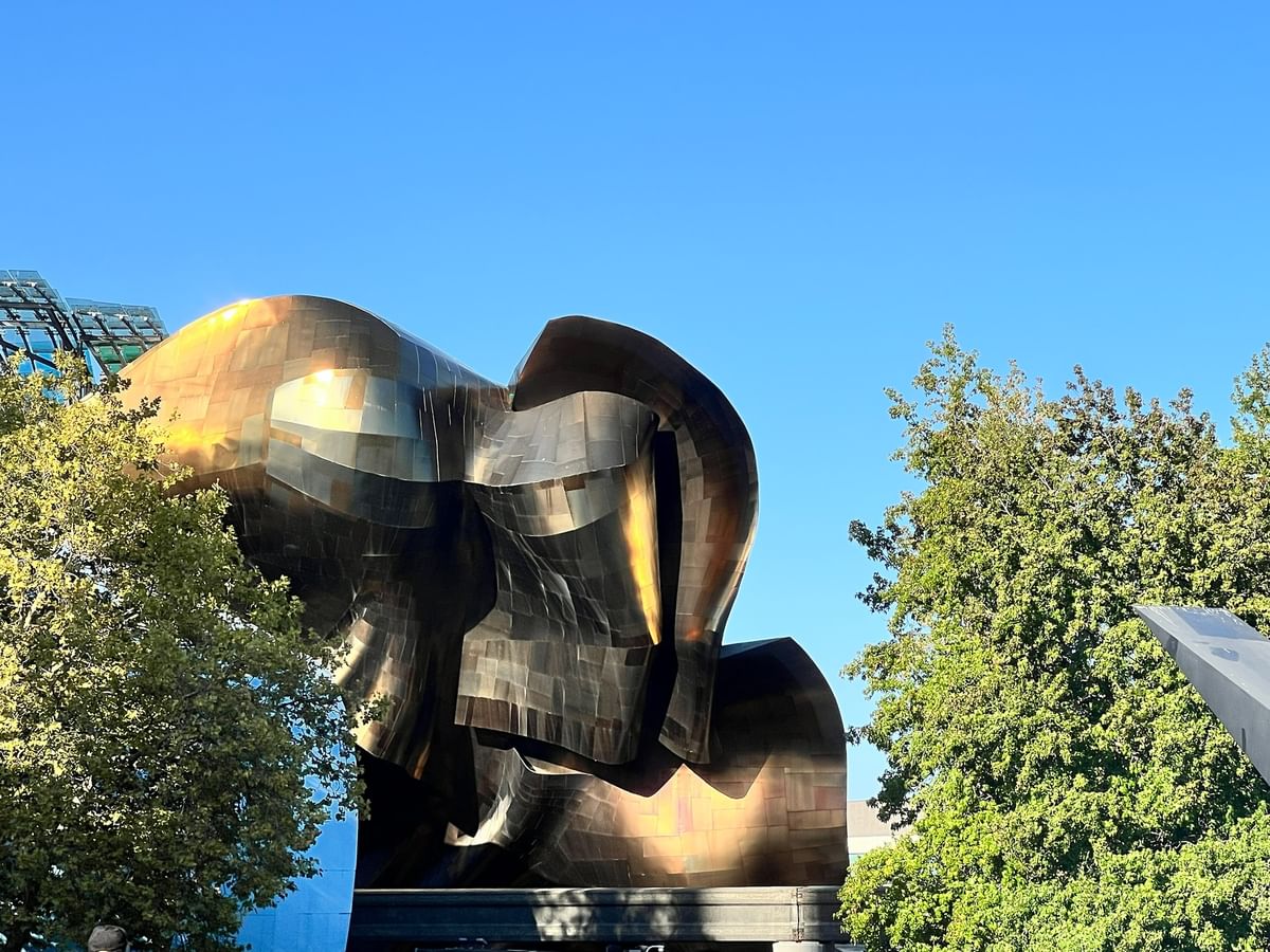 Modern metallic sculpture surrounding green trees under a bright blue sky,near Warwick Seattle