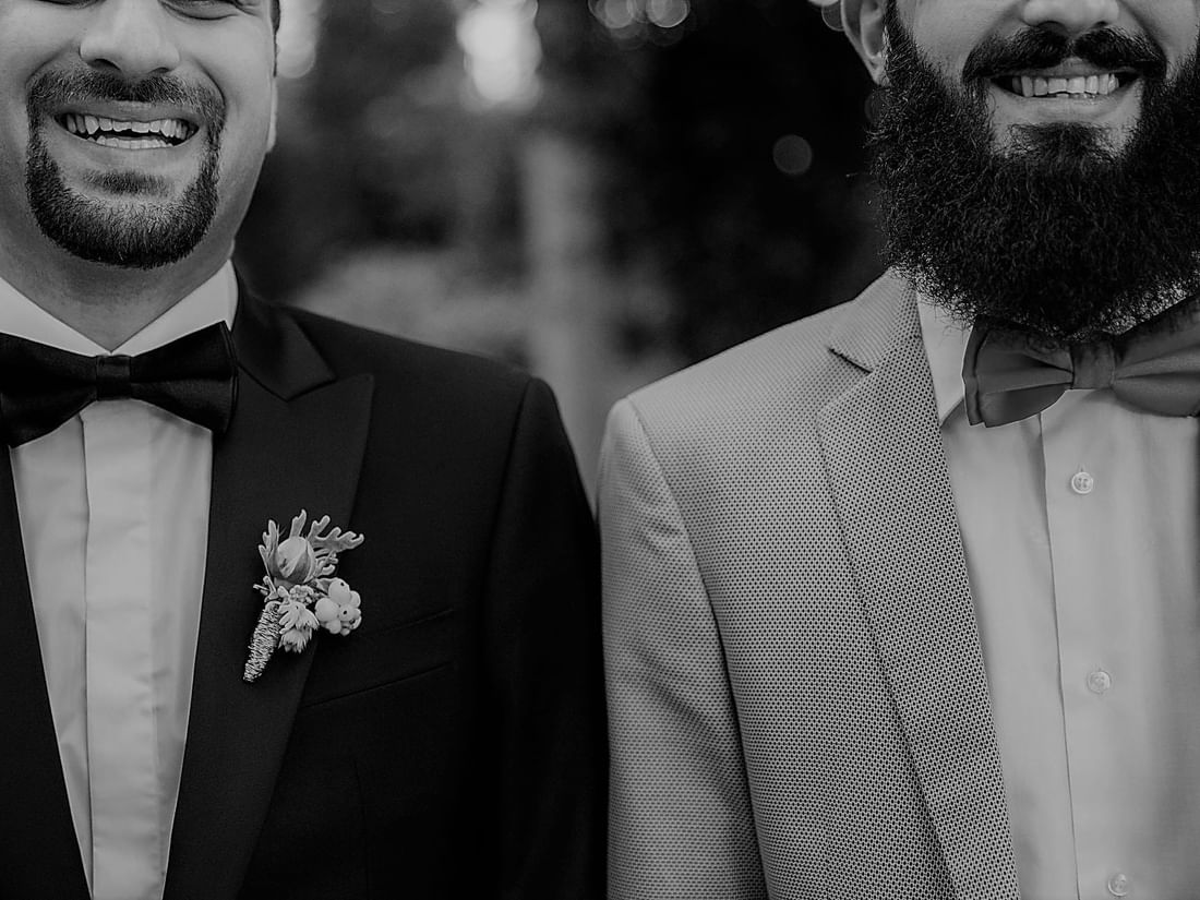 Black-and-white close-up of two grooms smiling on their wedding day at The Sebel Mandurah
