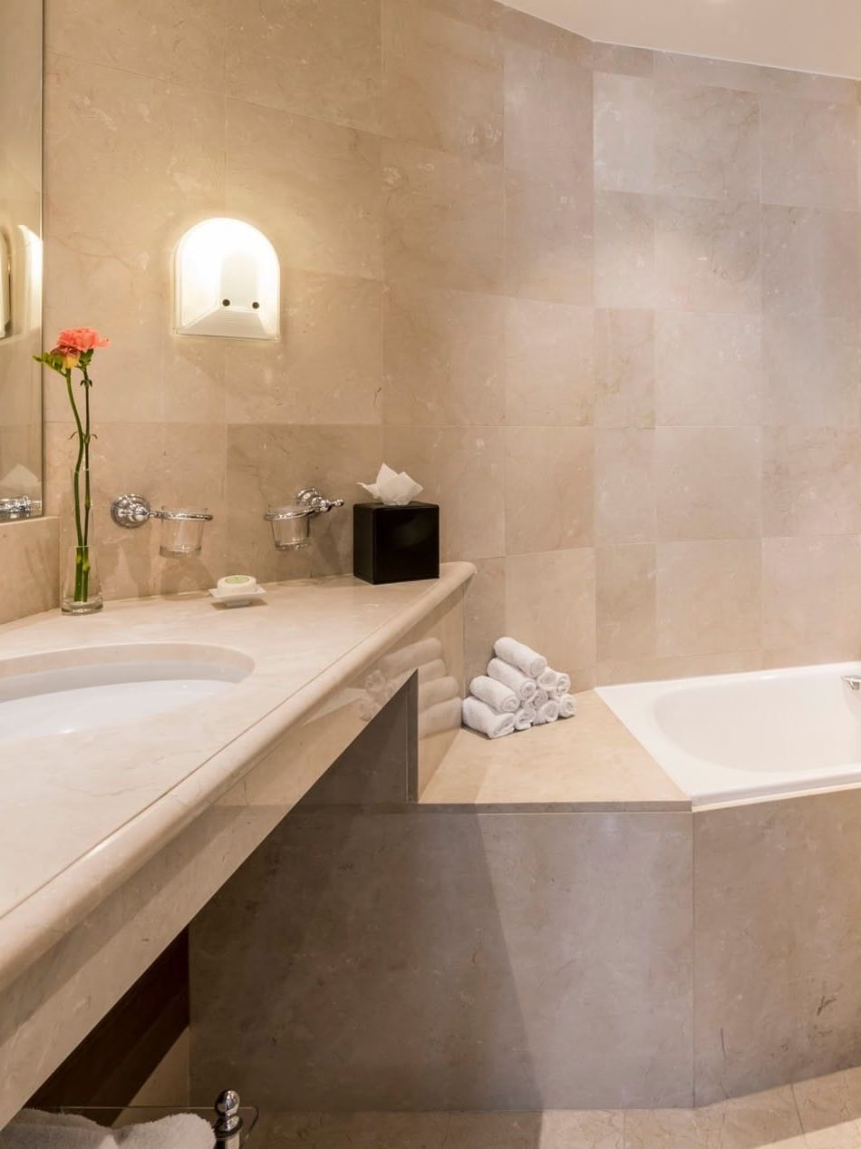 Junior Suite bathroom featuring a marble vanity with a mirror and bathtub at Warwick Grand Place Brussels