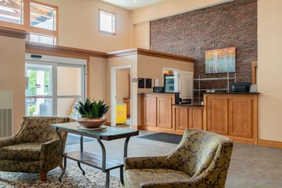 Bright lobby lounge area featuring wooden accents, two patterned chairs, and front desk at White River Inn and Suites