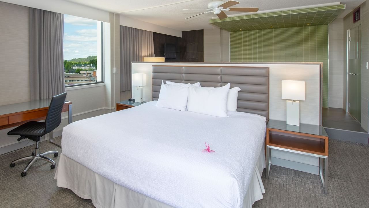 A hotel suite with a king bed, a desk, a chair, and a large window.