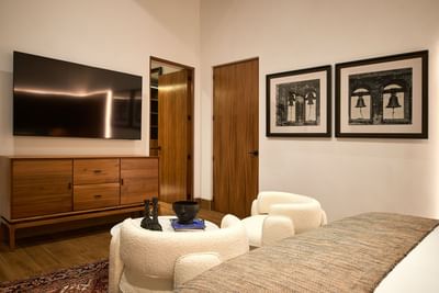 Cozy bedroom with a TV, a wooden cabinet, and two white armchairs at Singular Signature Residences