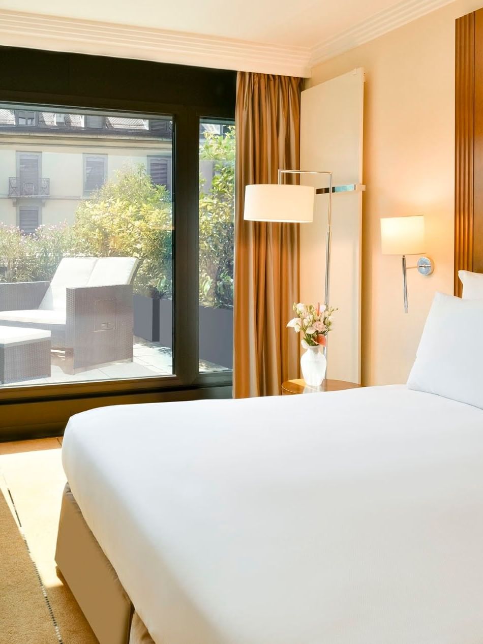 Deluxe Terrace Room with a bed by a glass door leading to a sunlit terrace at Warwick Geneva