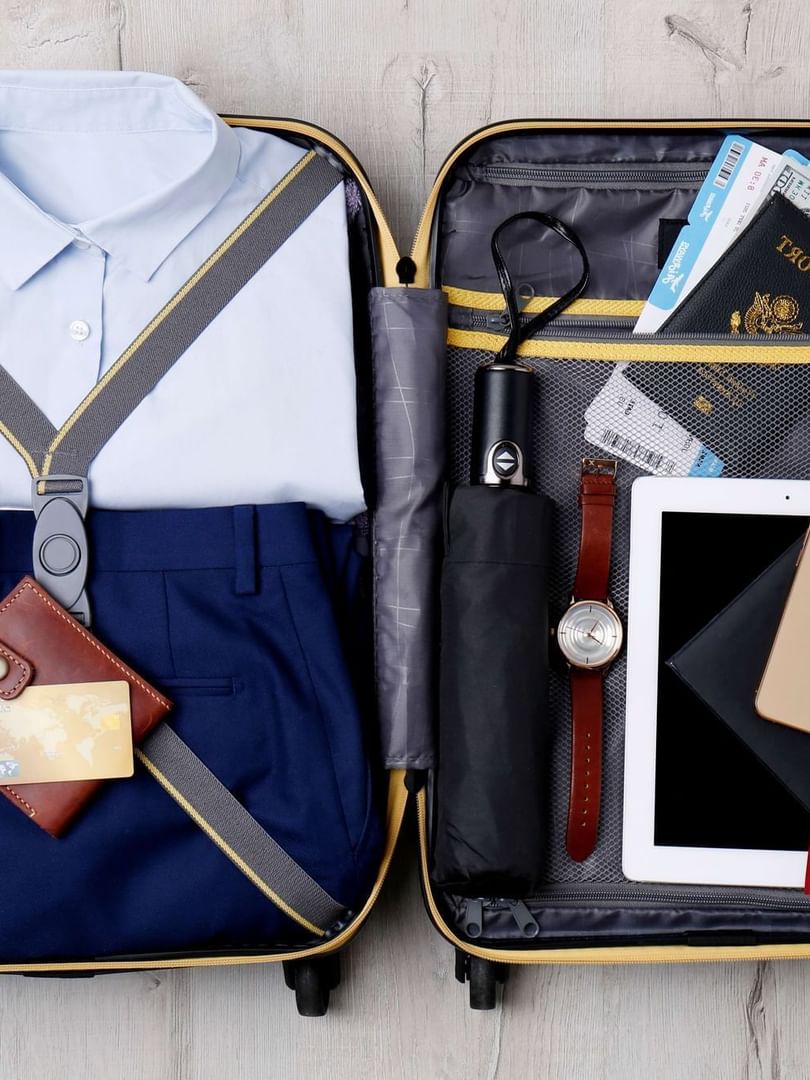 Organized suitcase with clothes placed by travel essentials, tech, and documents at Warwick Hotels & Resorts