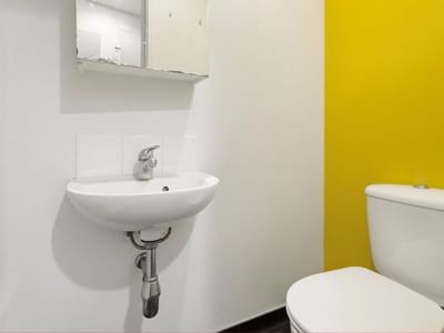 White sink and toilet in a small bathroom with yellow accent wall at Student Living Auckland Anzac.