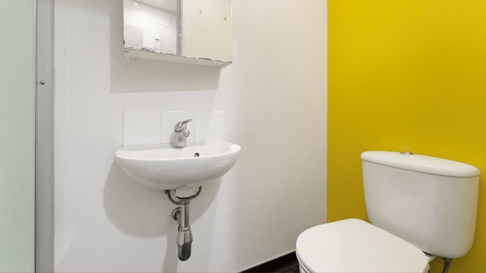 White sink and toilet in a small bathroom with yellow accent wall at Student Living Auckland Anzac.