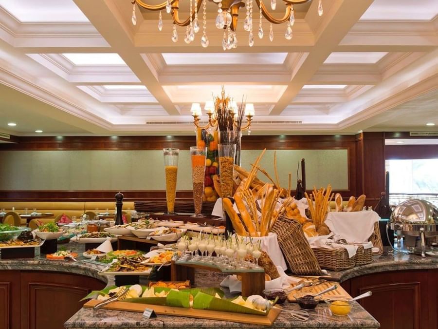Freshly baked bread in wicker baskets by appetizers, under a coffered ceiling at Warwick Doha Hotel