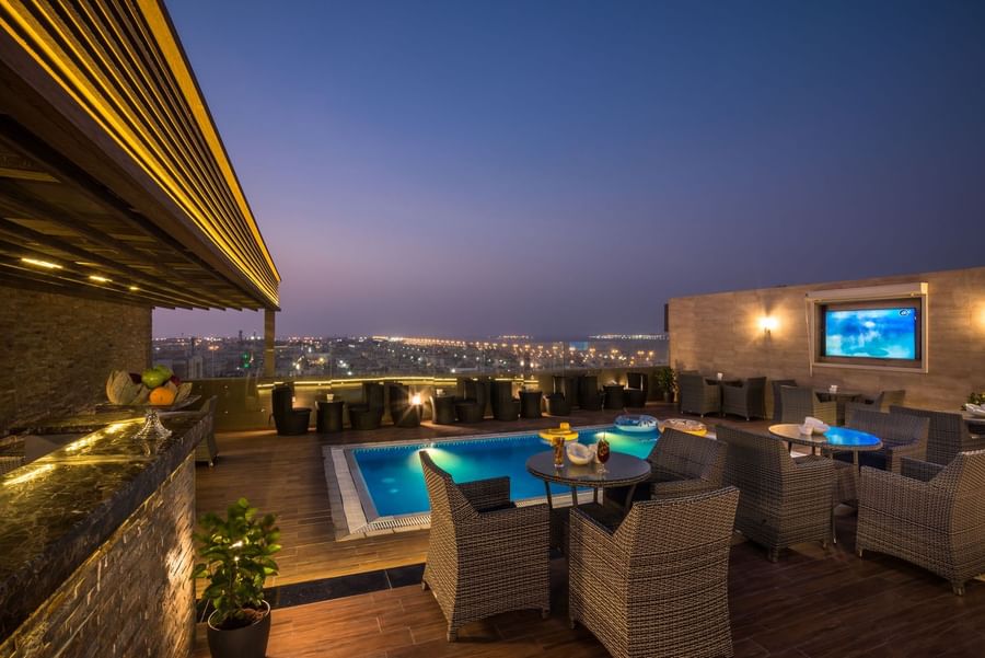 Rooftop pool featuring wicker chairs by tables under the night sky near the bar in Sky View Café at Naviti By Warwick Dammam