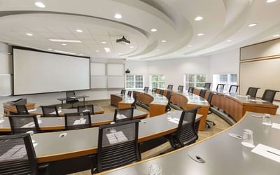 Curved wooden desks & mesh chairs facing a projection screen in Elm Room Amphitheatre at Spencer Hotel & Conference Centre