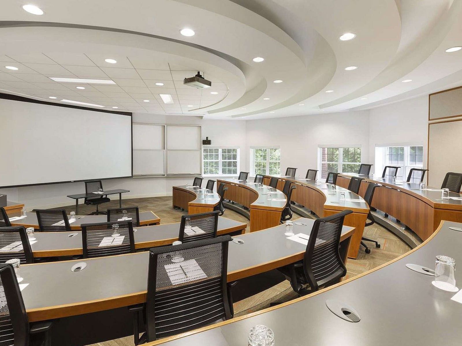 Curved wooden desks & mesh chairs facing a projection screen in Elm Room Amphitheatre at Spencer Hotel & Conference Centre