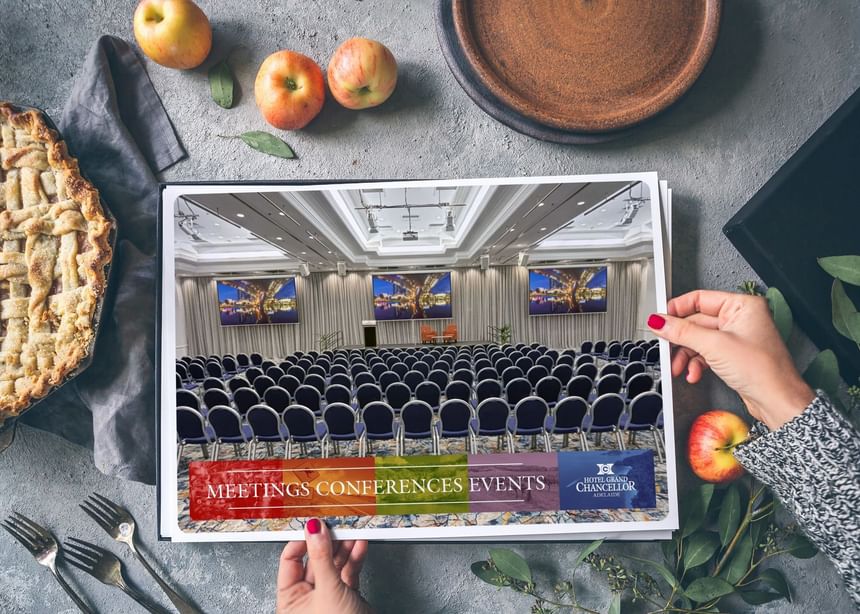 Hands hold a brochure showing a meeting room at Hotel Grand Chancellor Adelaide.
