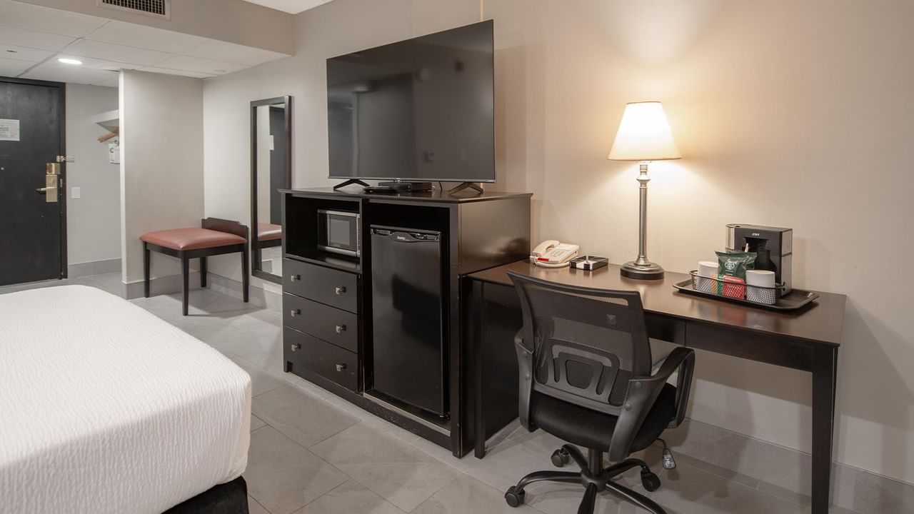 Hotel room with desk, chair, flat-screen TV, and mini-fridge.