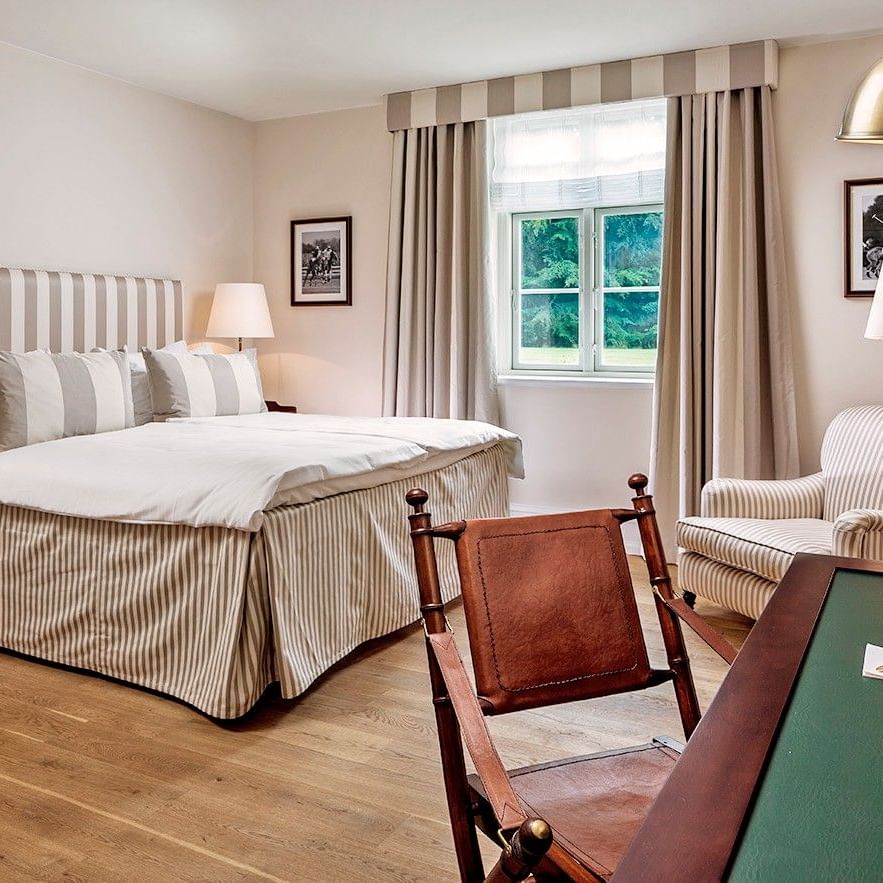 Superior room featuring striped bedding and curtains with leather chair and desk at Warwick Denmark