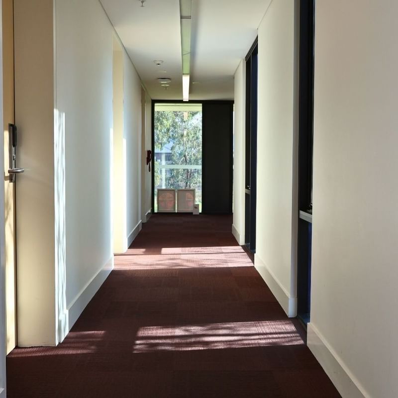 Long hallway with white walls, red carpet, and room doors at La Trobe University.