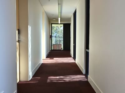 Long hallway with white walls, red carpet, and room doors at La Trobe University.