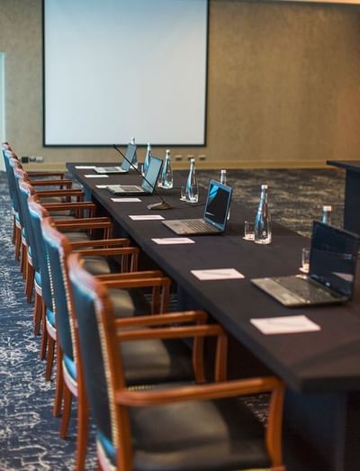 Table set-up with laptops, water bottles, and a projector screen in Neptune at Hotel Los Delfines & Casino