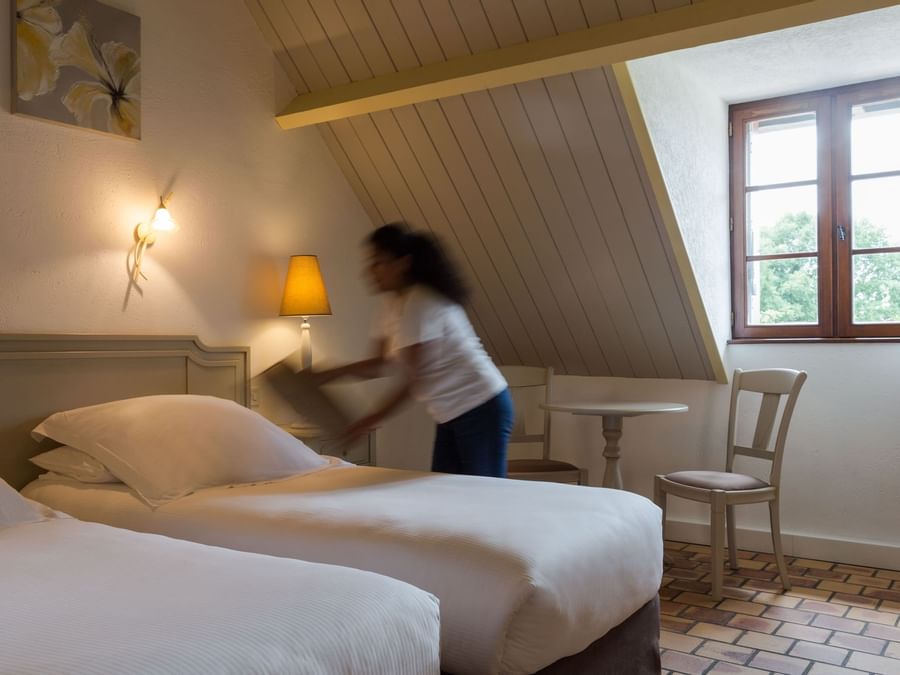 A maid preparing a bed in a room at L'Oree des Chenes
