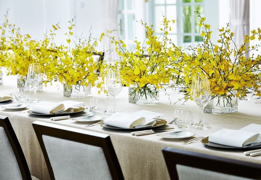 Dining area featuring a long table adorned with yellow floral centerpieces & set-up in the Pool House at Park Hyatt Saigon