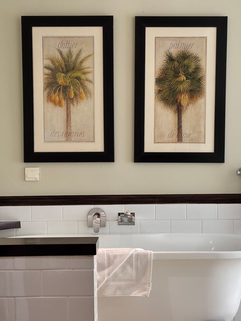 Bathroom with white bathtub, palm tree artwork, and towels at Warwick Le Lagon - Vanuatu, Efate.