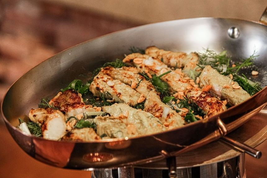 Stainless steel pan filled with golden-brown grilled chicken strips, garnished with herbs in Square One at Park Hyatt Saigon