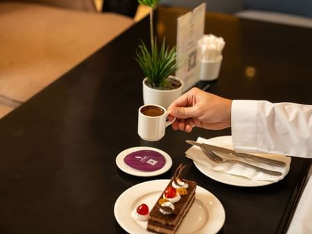 Hand serving coffee and dessert on table at Oasis Coffee Shop in Saja by Warwick Madinah.