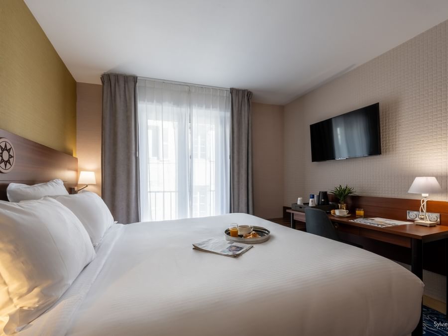 Chambre élégante avec lit, bureau et télévision au mur chez Hôtel Le Yachtman.