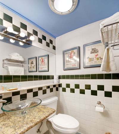 Standard Room bathroom at Chelsea Pines Inn with blue ceiling, green and white checkered tiles, and clear glass sink,