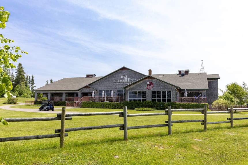 Wooden fence standing by an expansive green lawn in front of a rustic club building at Rodd Brudenell River Resort