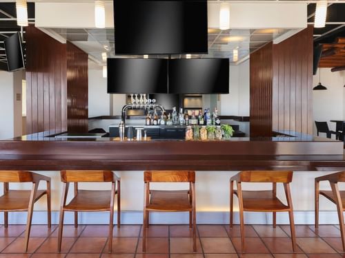 Sports Bar with a dark wood counter, empty wooden chairs, and TV screens at Hacienda del Mar Los Cabos