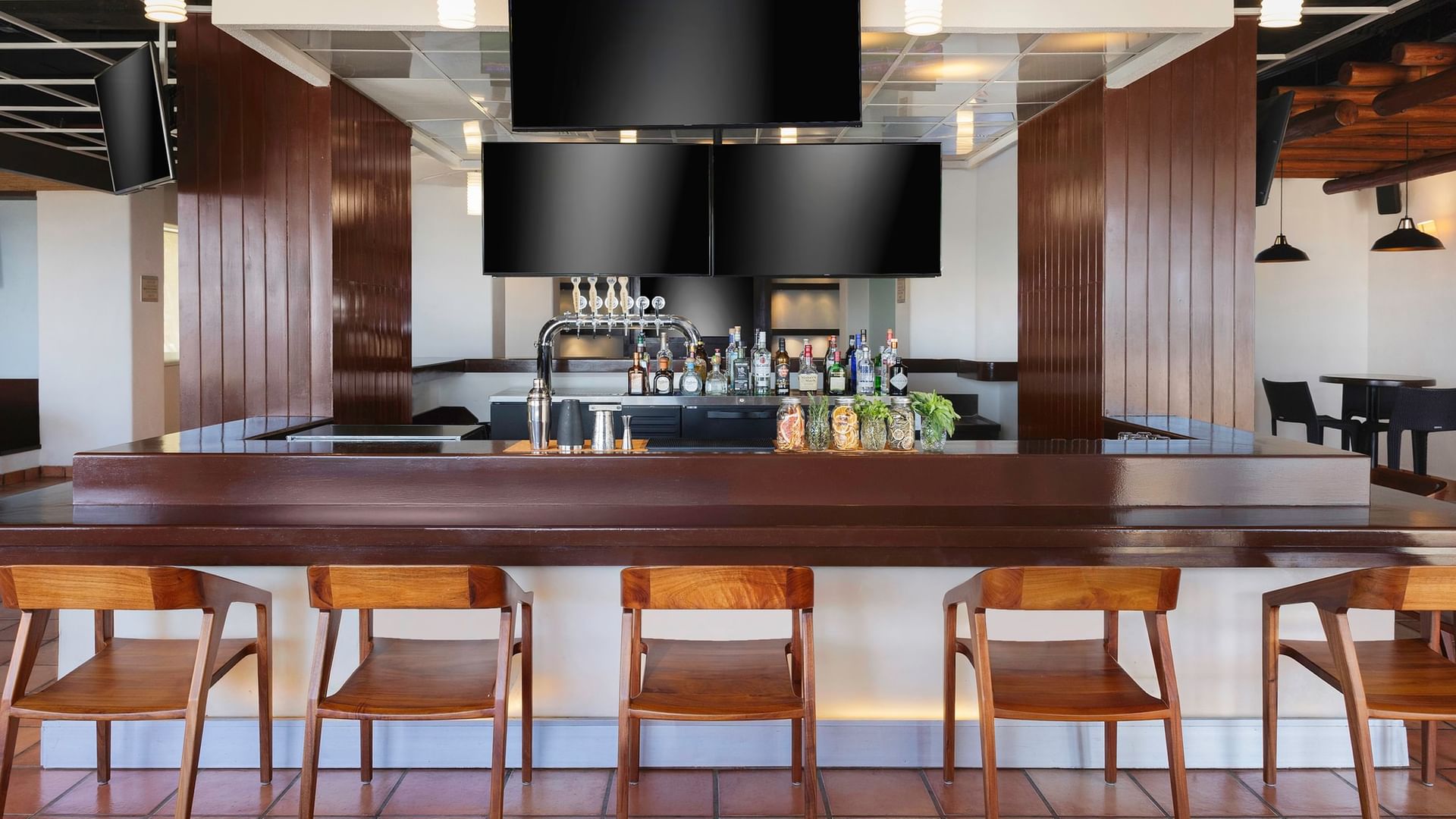Sports Bar with a dark wood counter, empty wooden chairs, and TV screens at Hacienda del Mar Los Cabos