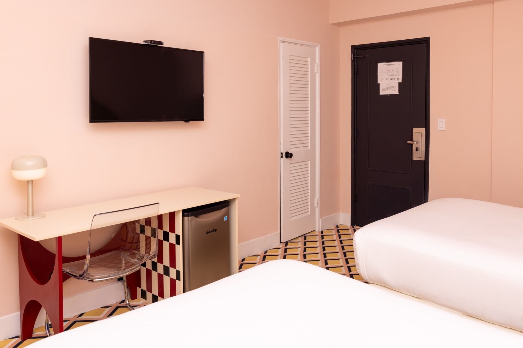 A hotel room with a double bed, desk, TV, and mini-fridge.