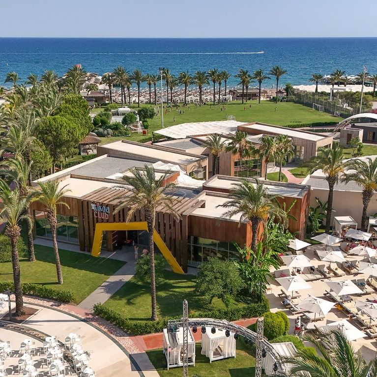 Titanic Deluxe Lara’daki Kikoa Kids Club’ın havadan görünümü; palmiye ağaçları, havuz ve Akdeniz manzarasıyla çocuklara özel bir tatil cenneti