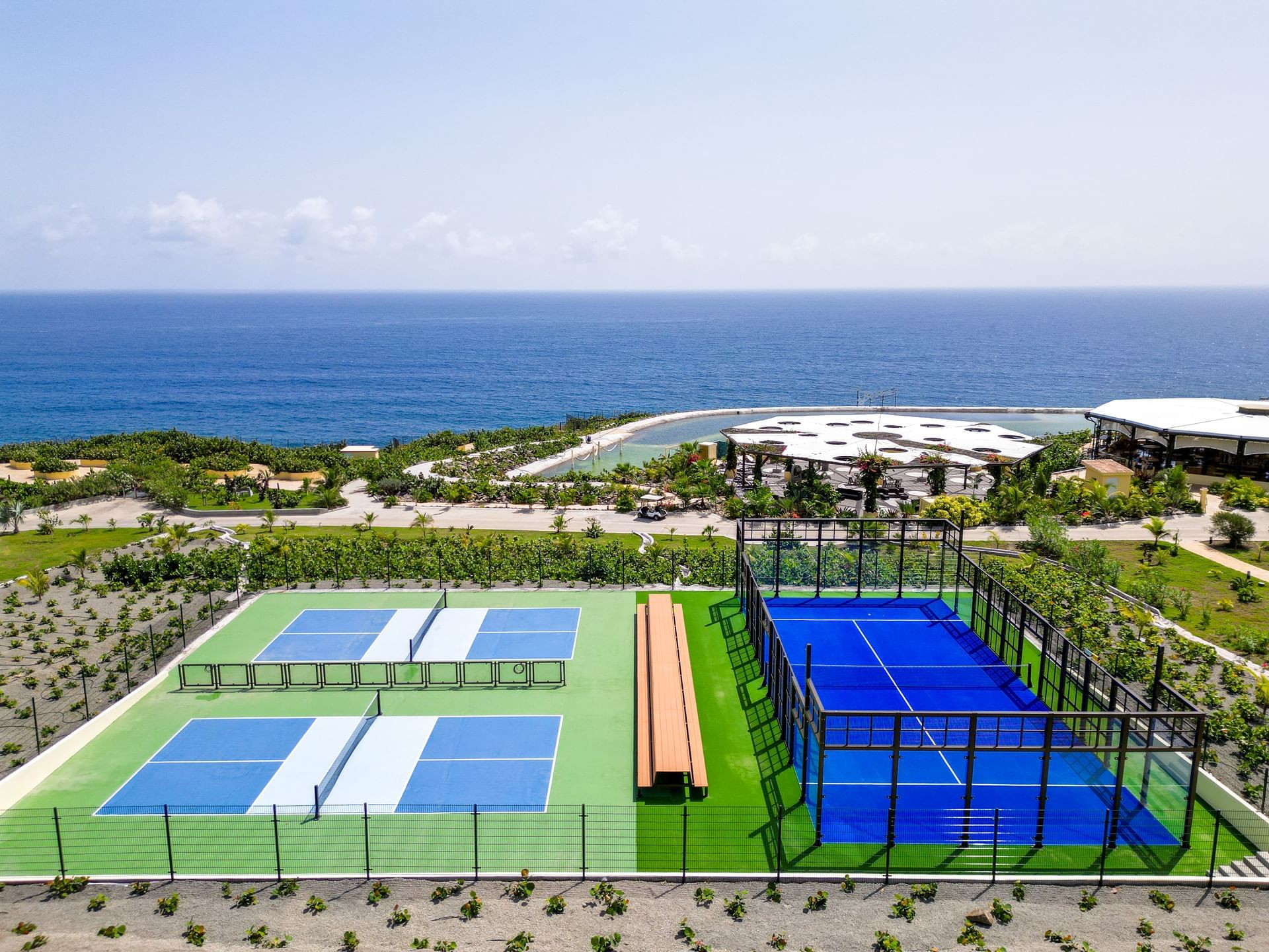 Panoramisch uitzicht op tennisbanen en een padelbaan aan de oceaan, omringd door weelderig groen nabij Golden Rock Resort