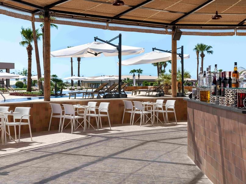 Outdoor bar with patio tables and chairs, umbrellas, and a pool view.