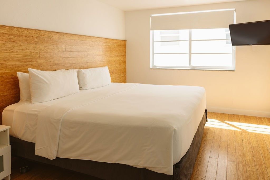 A hotel room with a large bed, wooden headboard, and window with a TV mounted on the wall.