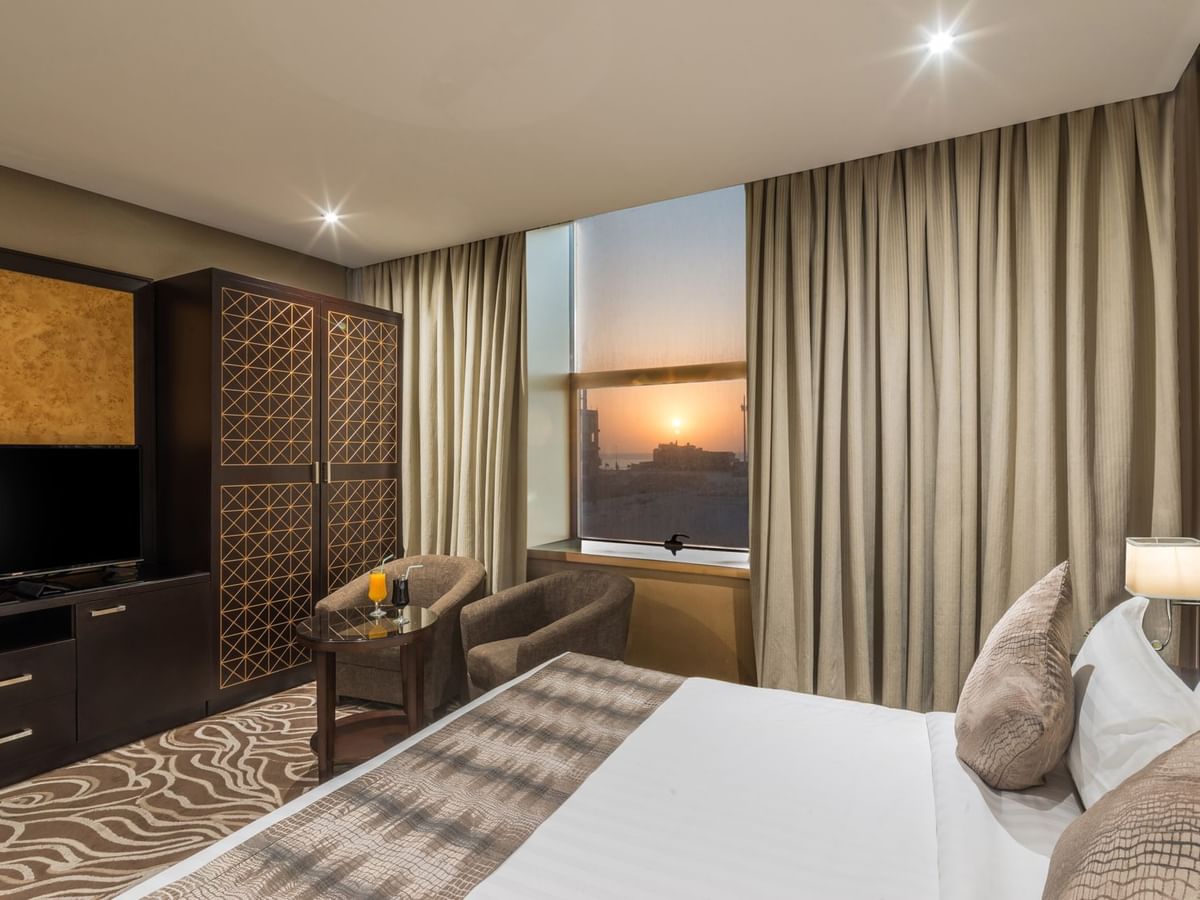 غرفة أنيقة تضم سريرًا ومنطقة جلوس مريحة وإطلالة على غروب الشمس في فنادق ومنتجعات وارويك