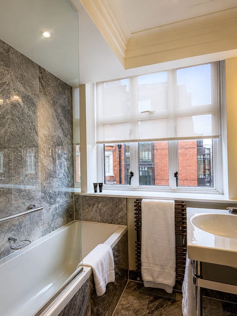 White sink by a chrome faucet under a mirror near a marble bathtub with a glass screen at Warwick Hotels & Resorts
