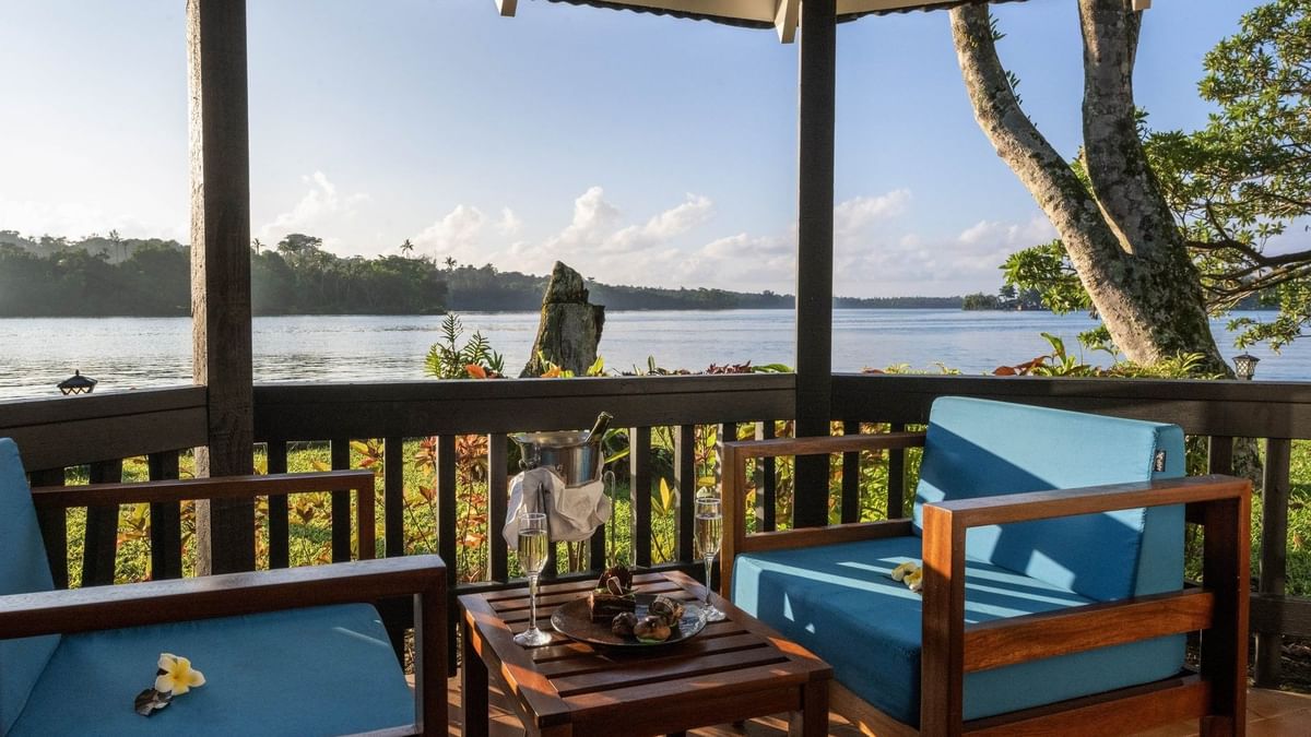 Balcony with blue chairs and table set with champagne and sweet treats in Lagoon Bungalow at warwick le lagon-vanuatu