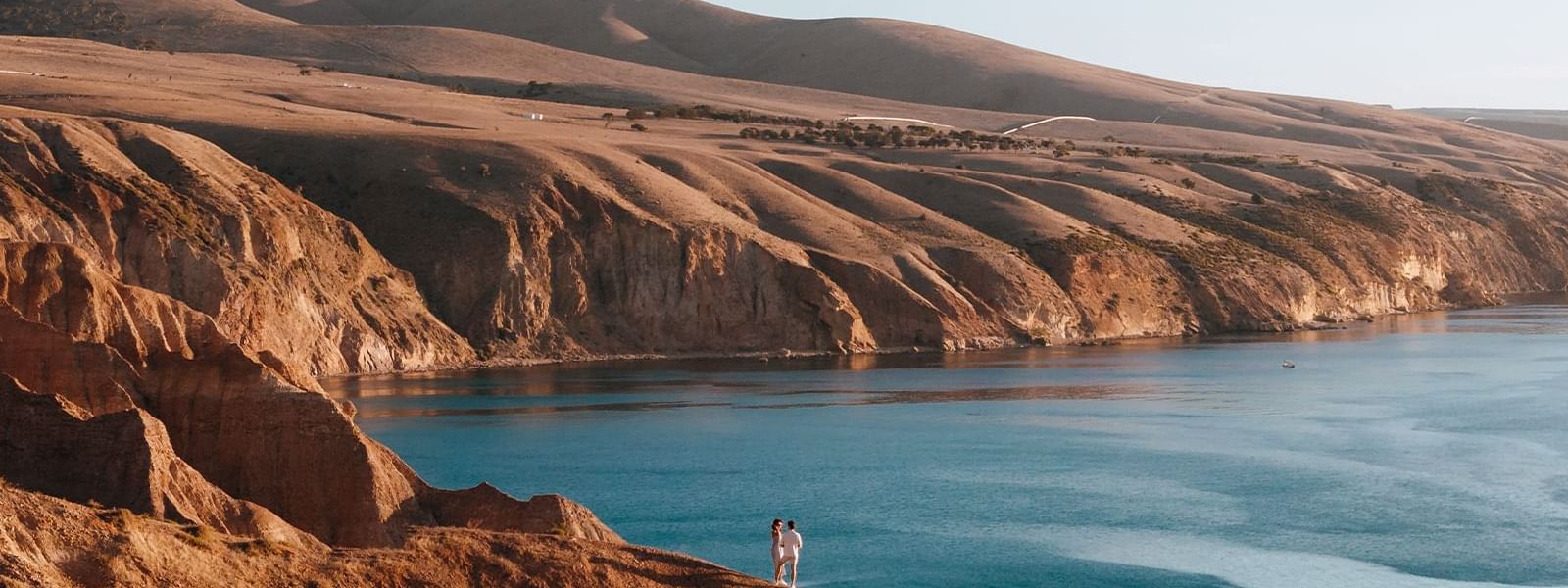 Couple on a cliff overlooking blue ocean and rolling hills near Ibis Adelaide