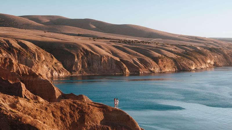 Couple on a cliff overlooking blue ocean and rolling hills near Ibis Adelaide