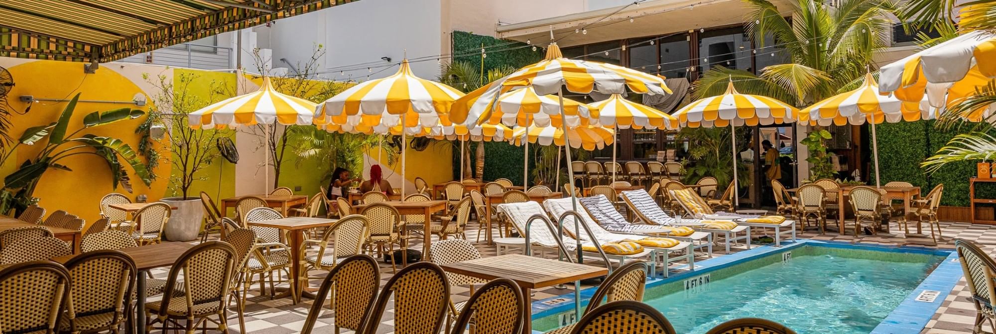 A poolside area with yellow and white umbrellas, lounge chairs, and tables and chairs.