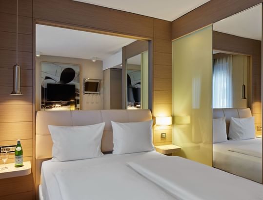 Queensize-Bett, großer Spiegel und eine Nachttischlampe im Standardzimmer im Titanic Comfort Mitte