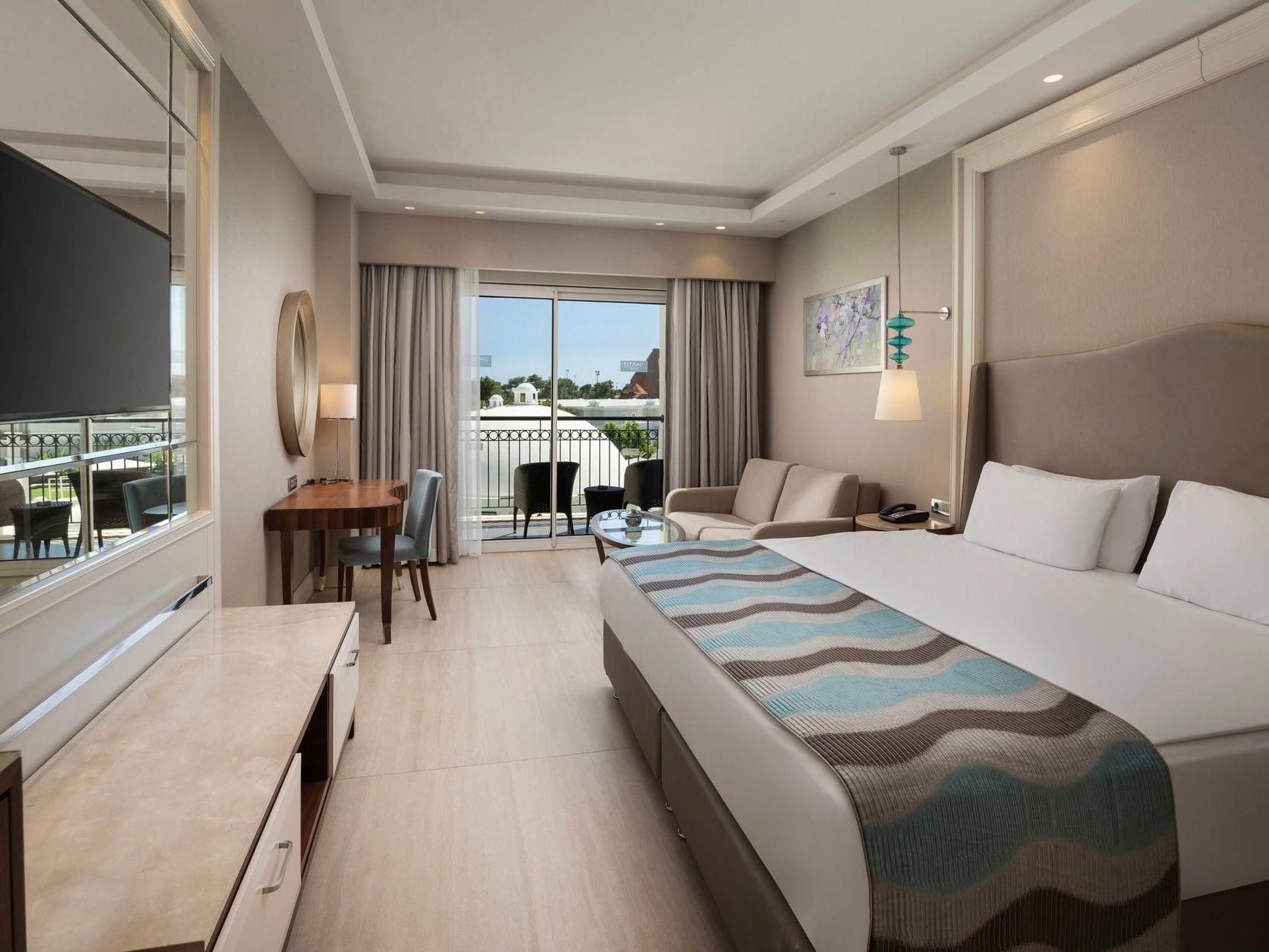 Modern guest room with king bed, balcony access, seating area, and contemporary furnishings at Titanic Deluxe Golf Belek