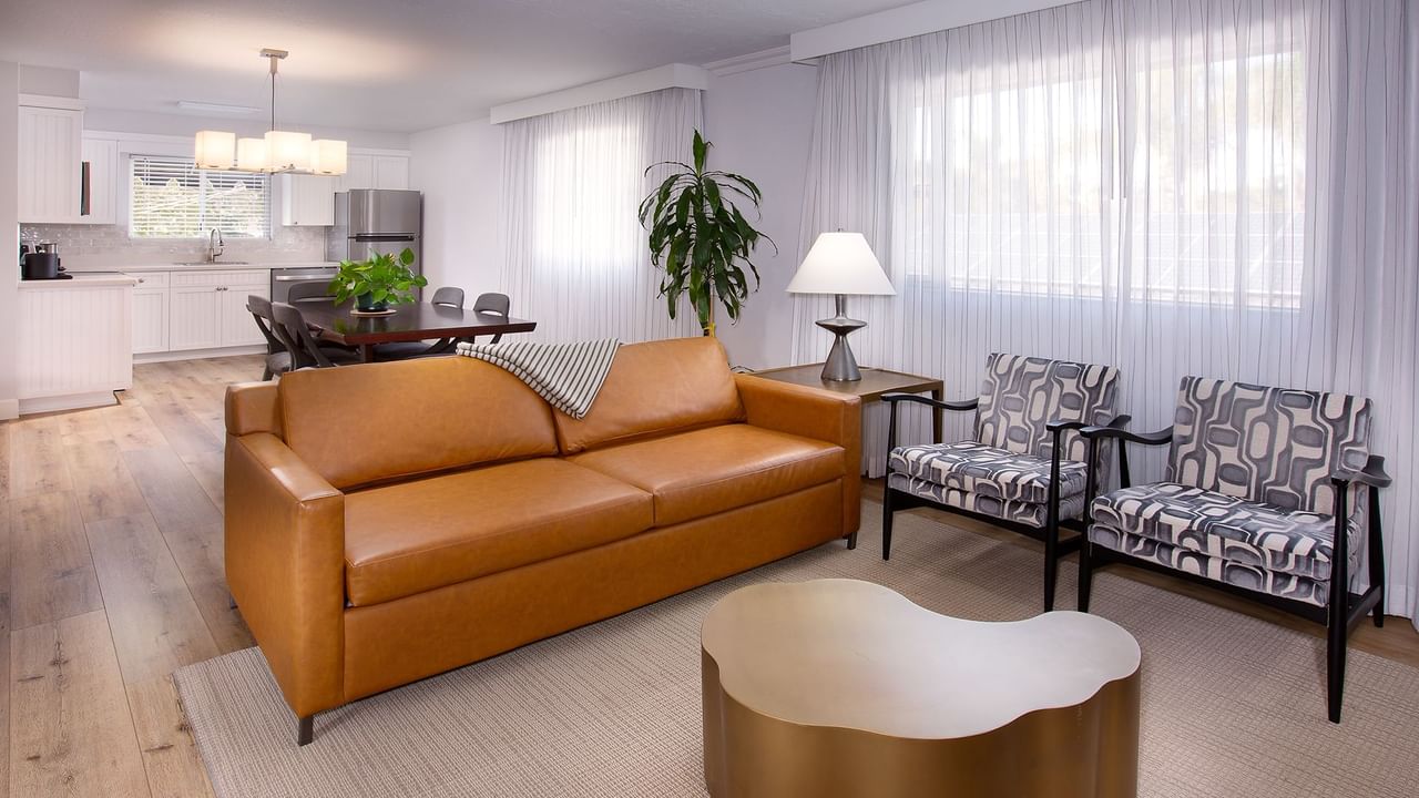 Living room with brown couch, two patterned chairs, wooden table, and a dining area in the background.