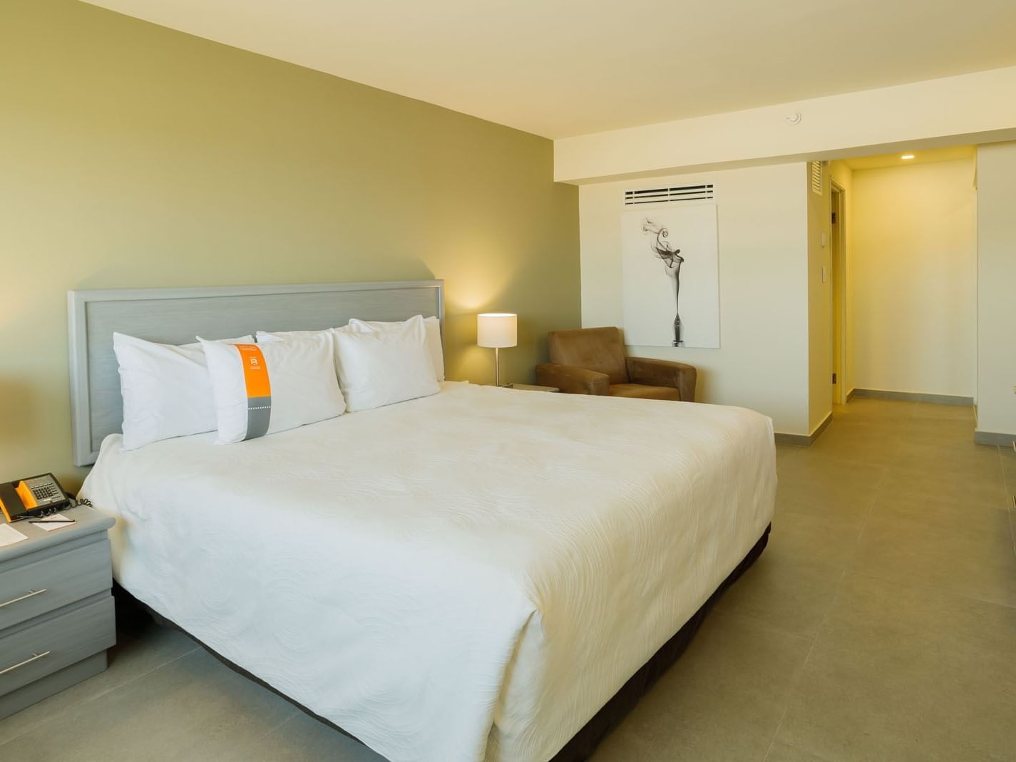 King Executive Suite at Real Inn Mexicali, featuring a plush brown armchair and minimalist art for a relaxing stay