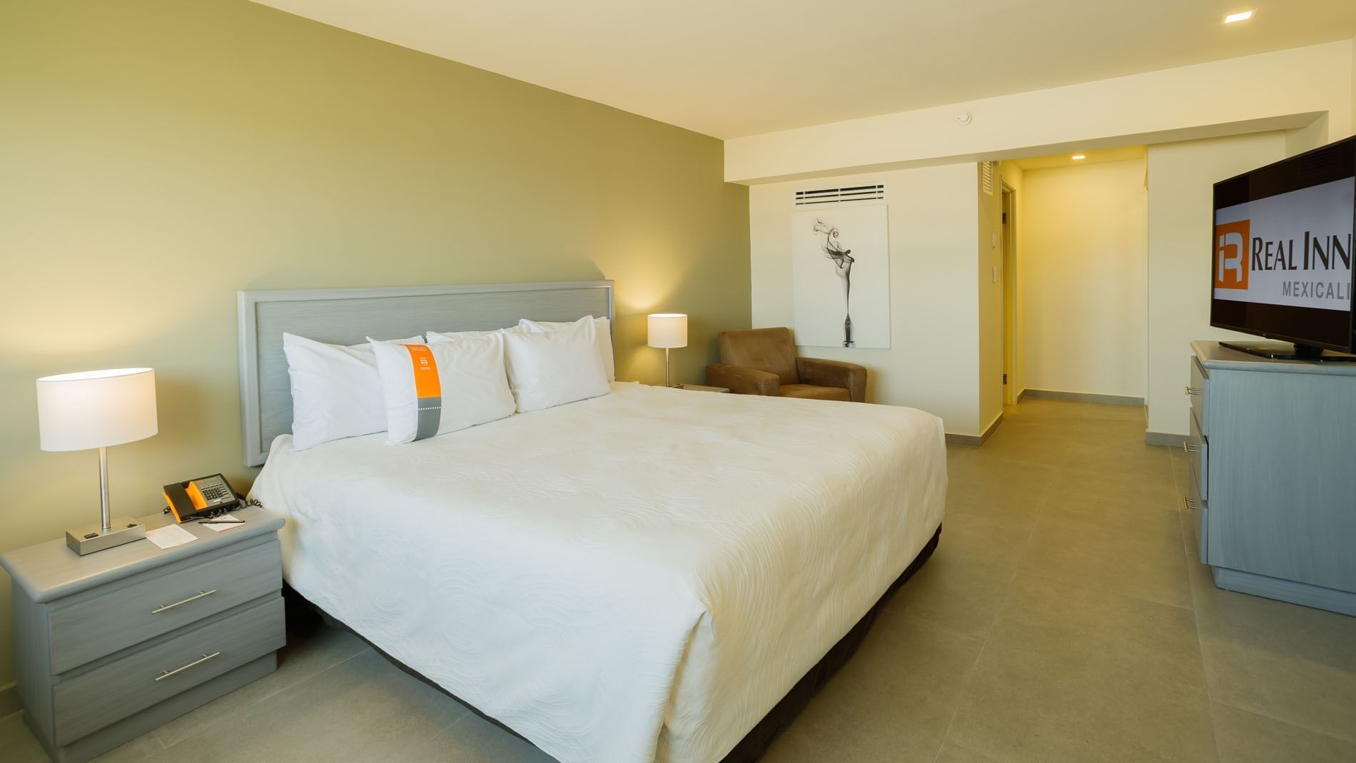 King Executive Suite at Real Inn Mexicali, featuring a plush brown armchair and minimalist art for a relaxing stay