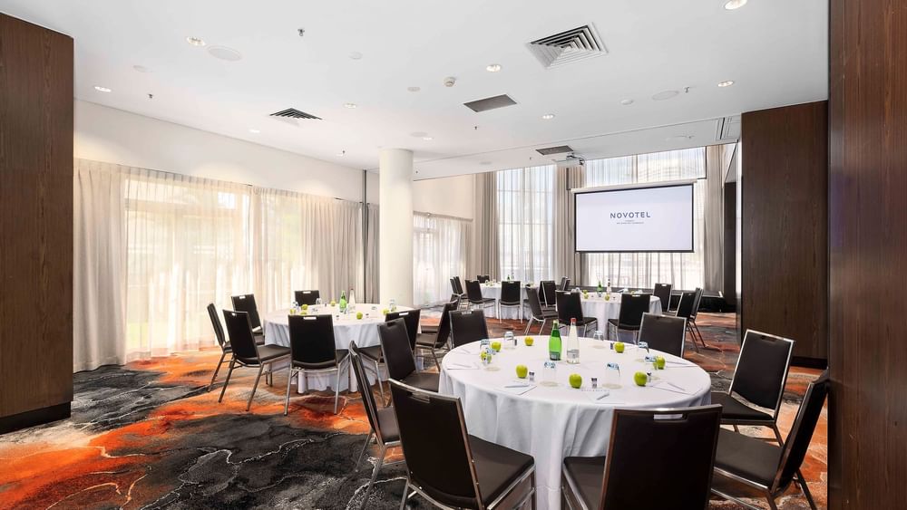 Cabaret set-up with a projector screen and carpeted floors in The Hunter Room 1-2 at Novotel Sydney on Darling Harbour