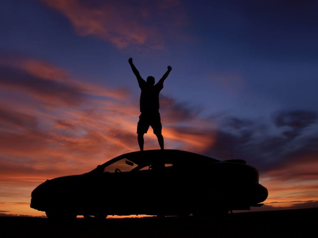 A man standing on a car watching the sunset